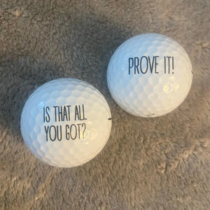 Two golf balls with humorous text on a textured surface