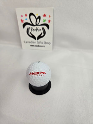 Golf ball with Masuta branding on a stand against a white background with a logo in the corner.